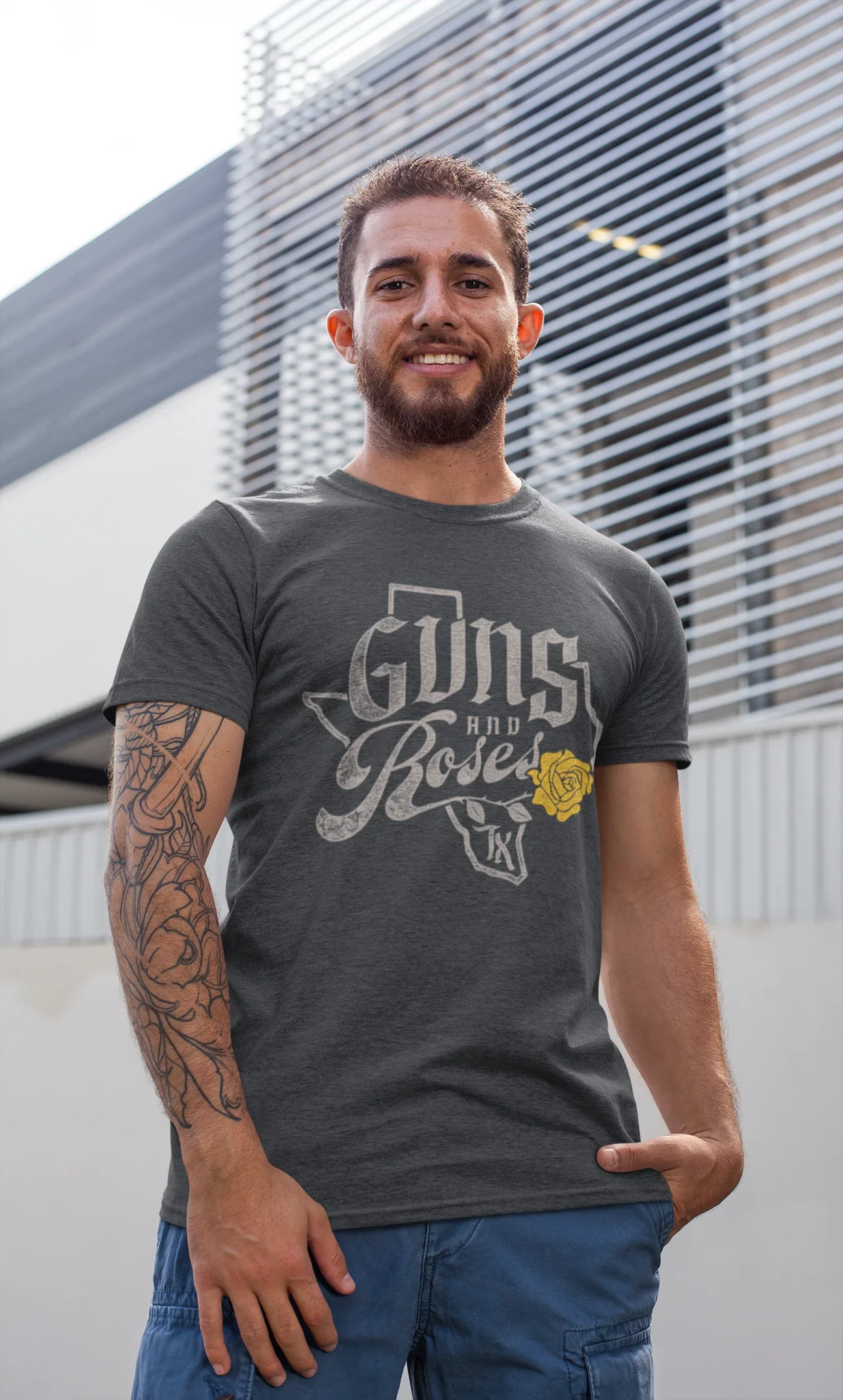 Man wearing a Guns and Roses Texas t-shirt standing outside with a tattooed arm and smiling.